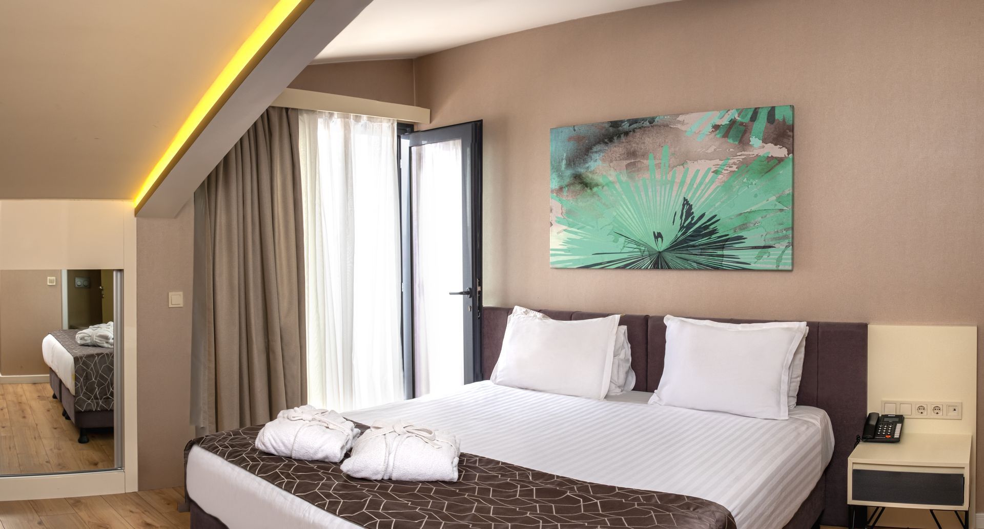 Hotel room with a bed, TV, small kitchen, and desk with chair. Walls are gray, bedspread is orange.