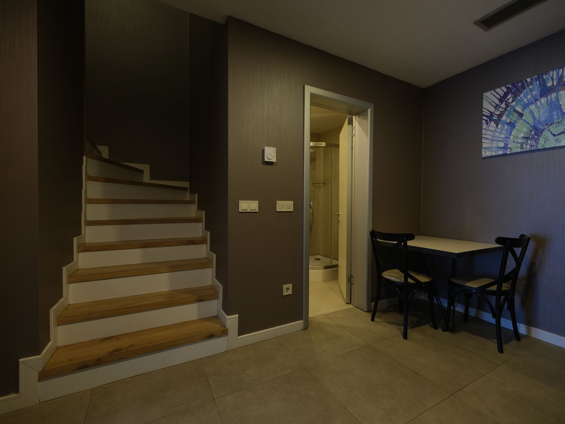 Interior of a small space with a staircase, dining table, and a door to a bathroom. The walls are dark.