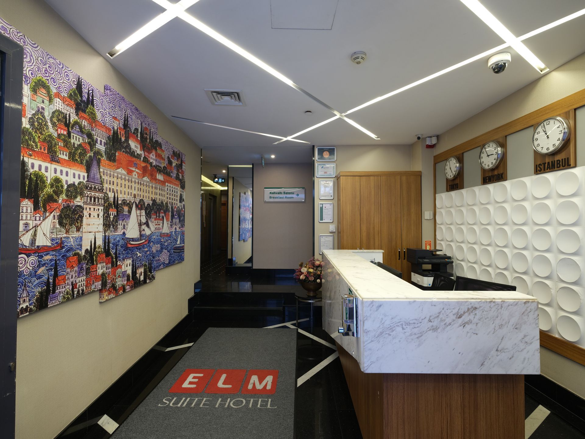 Hotel lobby with a reception desk. A large painting of a coastal city scene hangs on a wall.