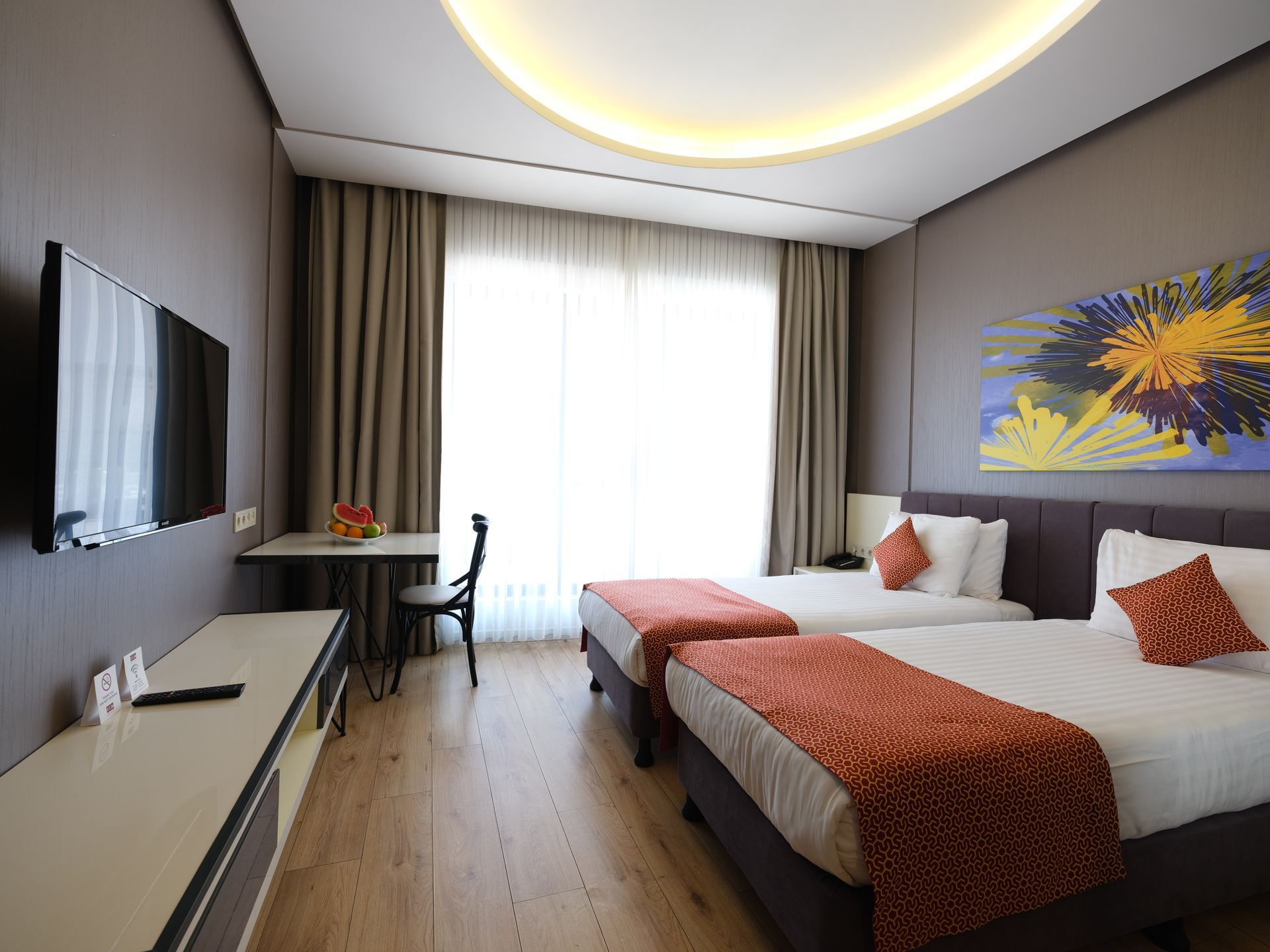 Hotel room with two twin beds, a desk, TV, and a large window with curtains. 