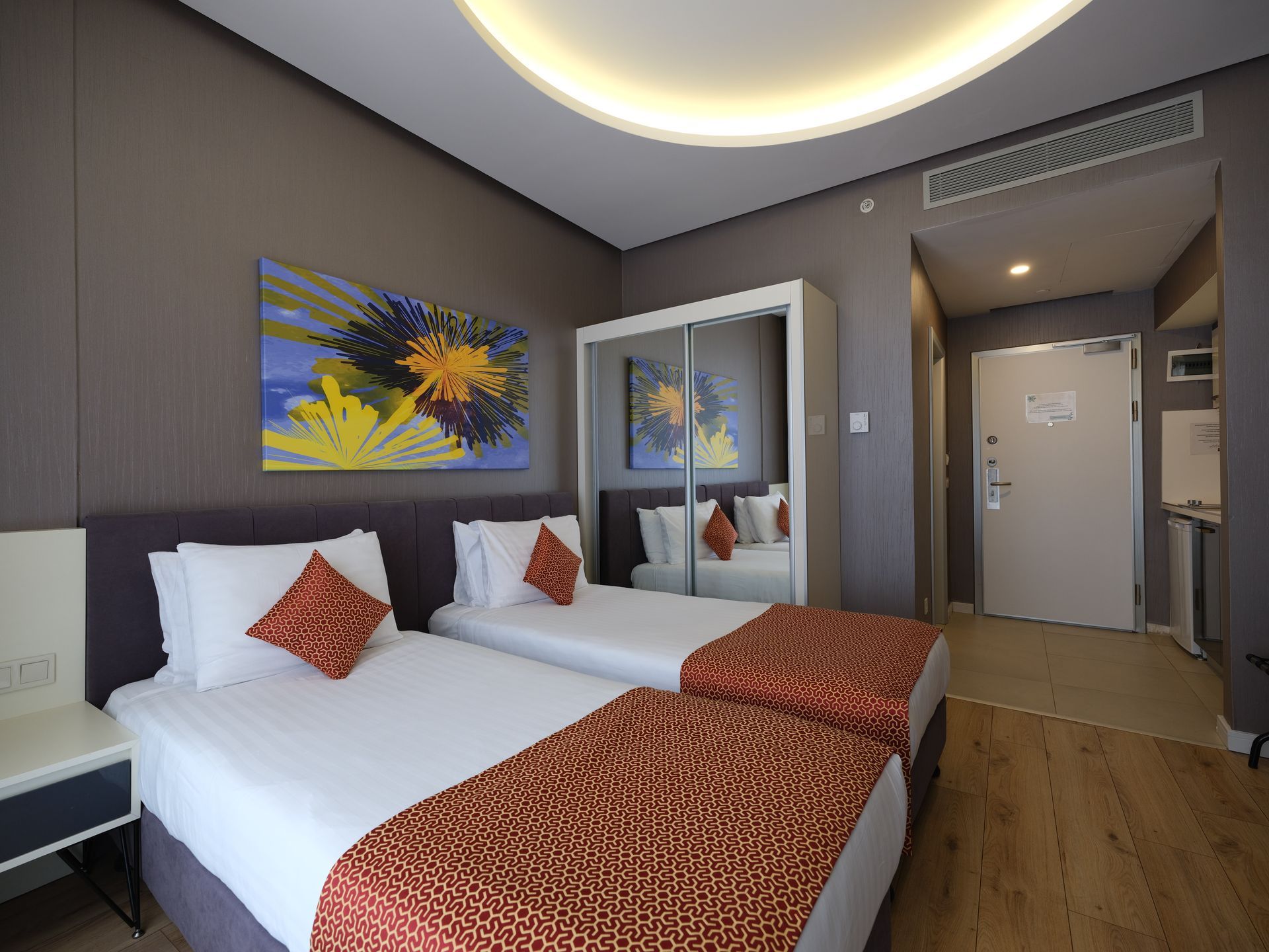 A hotel room with two twin beds, a painting, and a closet with a mirrored door.