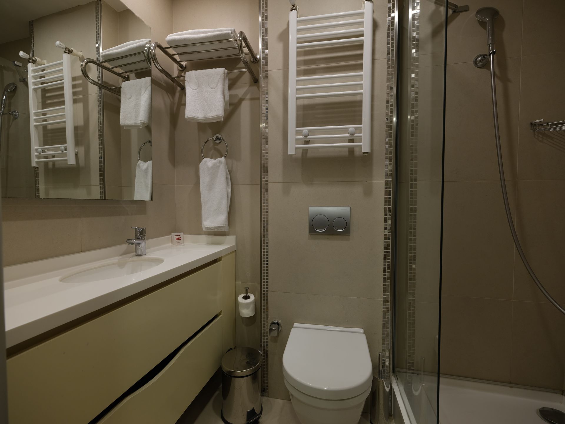 Bathroom with a white vanity, toilet, shower, and towel racks; neutral tones.