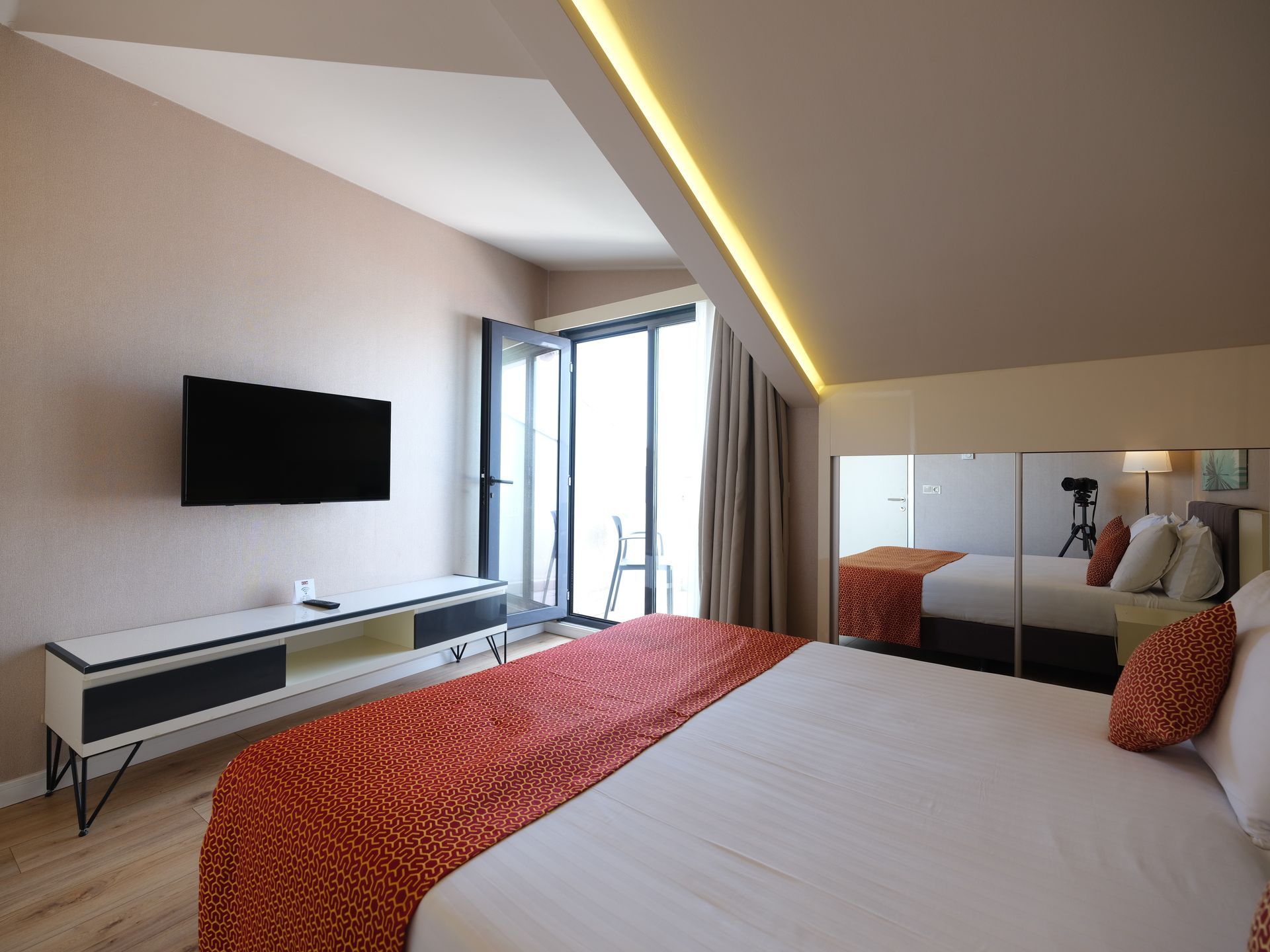 Bedroom with a large bed, TV, and balcony doors, with a large mirror reflecting the room.