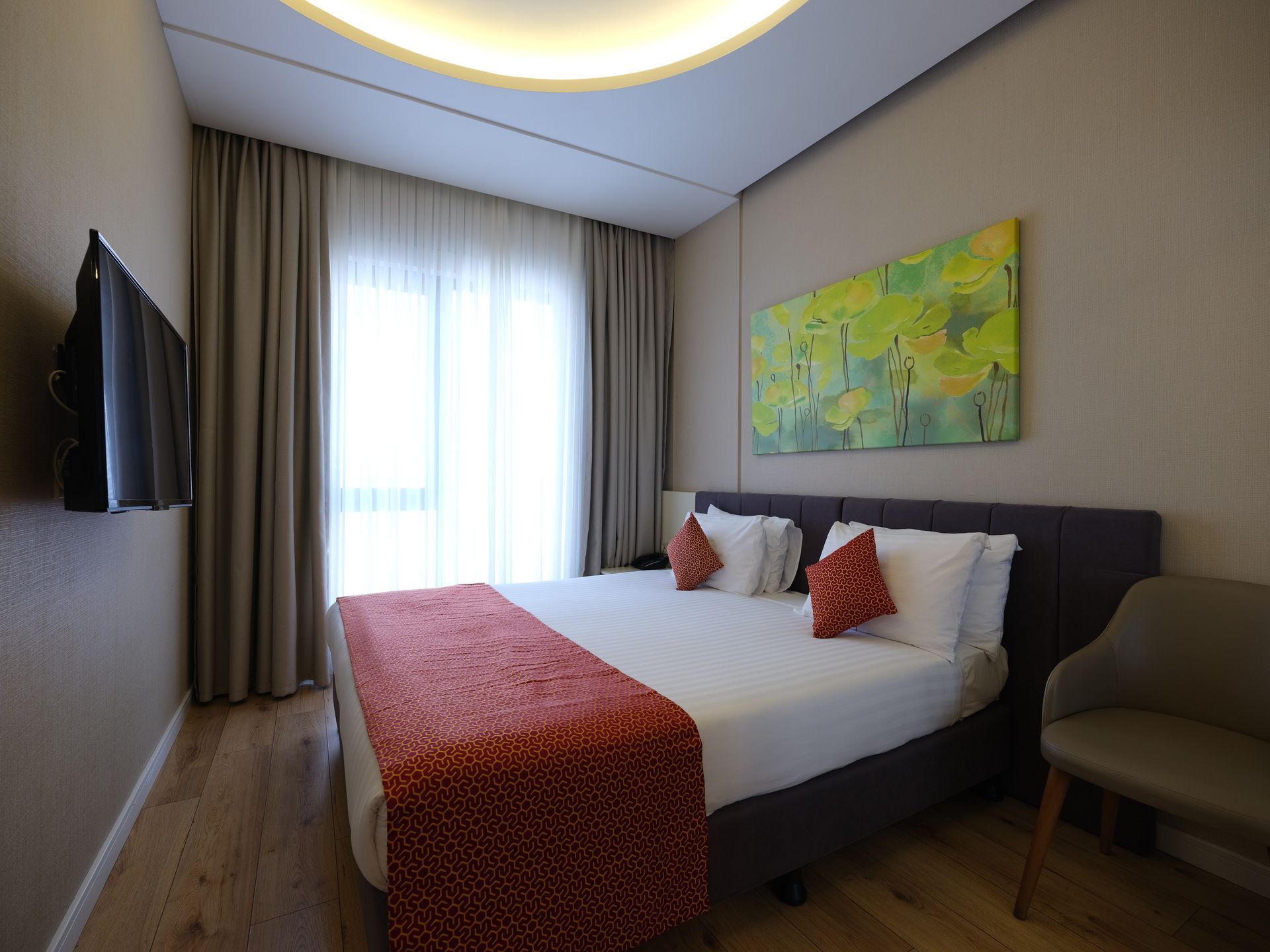 A hotel bedroom with a bed, TV, and artwork. 