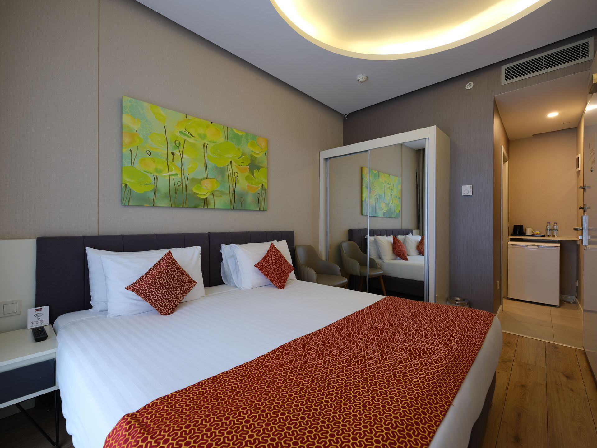 A hotel room with a large bed covered in white sheets and orange accents. 