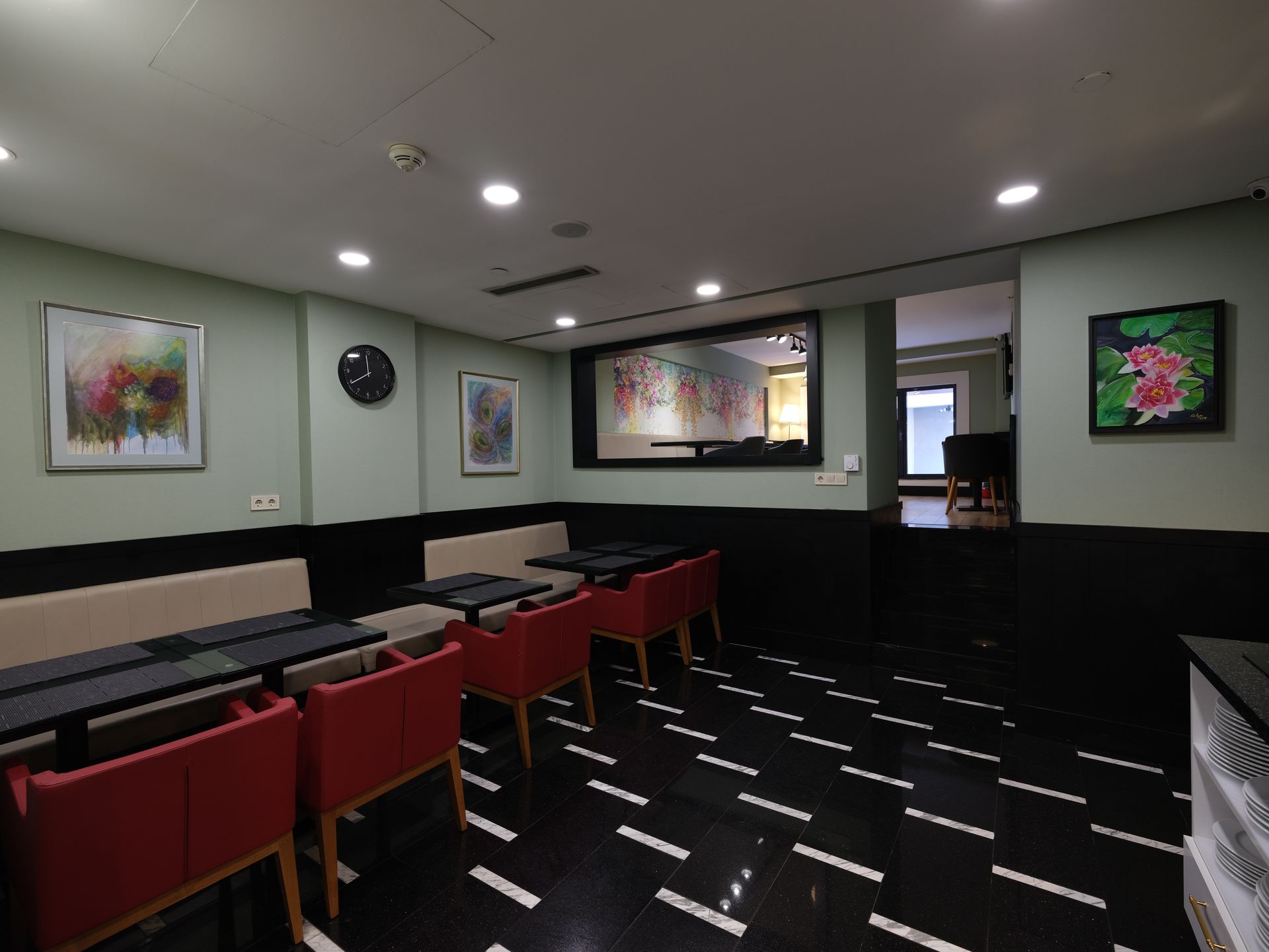 A restaurant interior with black and white tiled floor, red chairs, and a large mirror reflecting another room. 