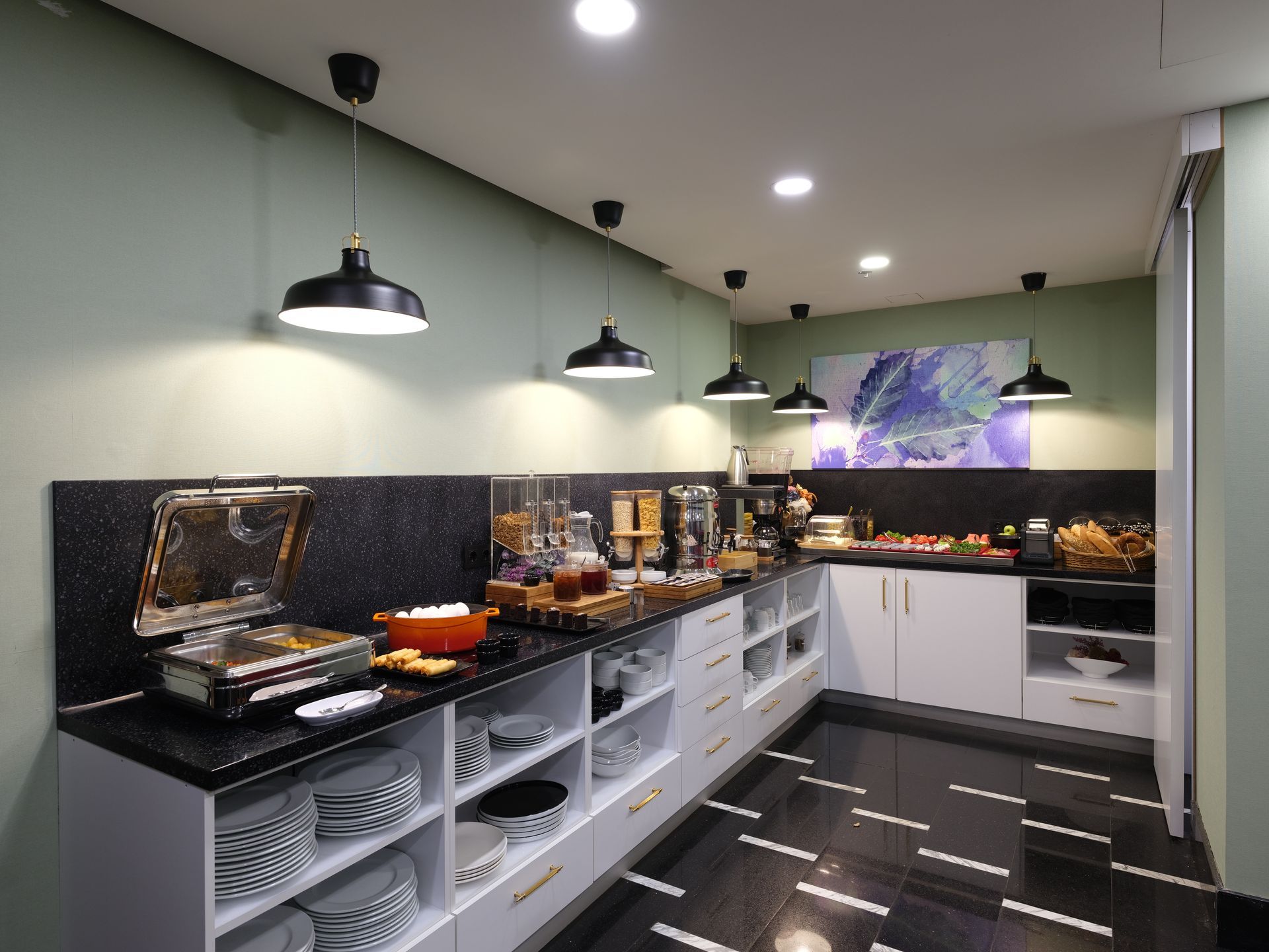 Breakfast buffet area with black and white countertops, white cabinets, and hanging black lamps. 