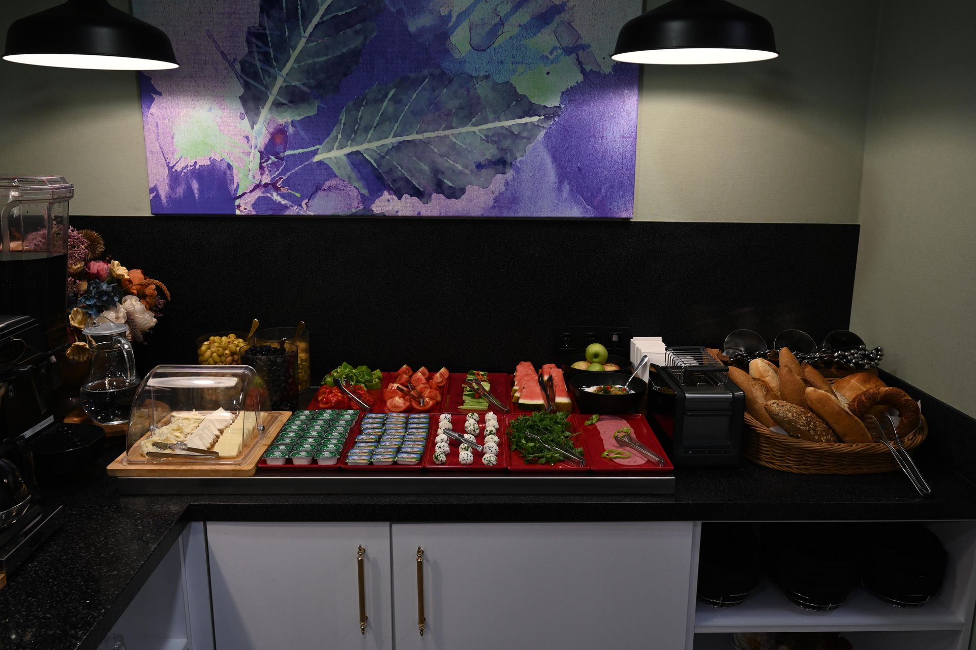 A buffet with various food items like cheese, tomatoes, bread, and watermelon, is set up on a countertop. 