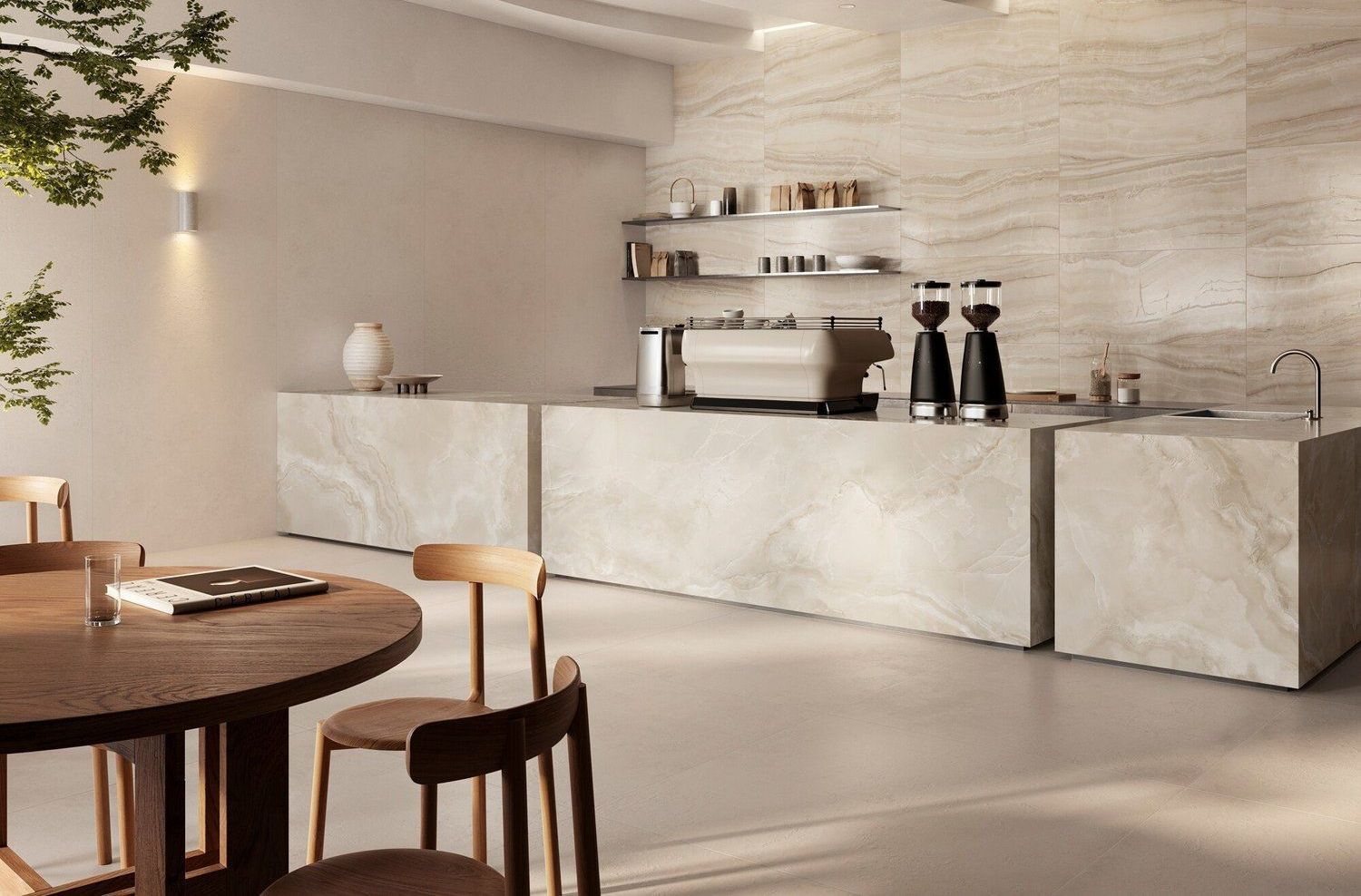 Interno minimalista di una caffetteria con bancone rivestito in pietra, macchina per caffè espresso, tavolo da pranzo in legno e sedie in una palette di colori neutri.