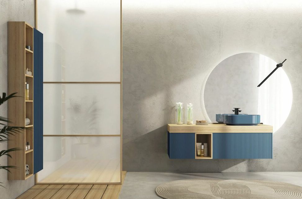 Bagno moderno con mobile lavabo blu a parete con dettagli in legno, specchio circolare e box doccia in vetro satinato.