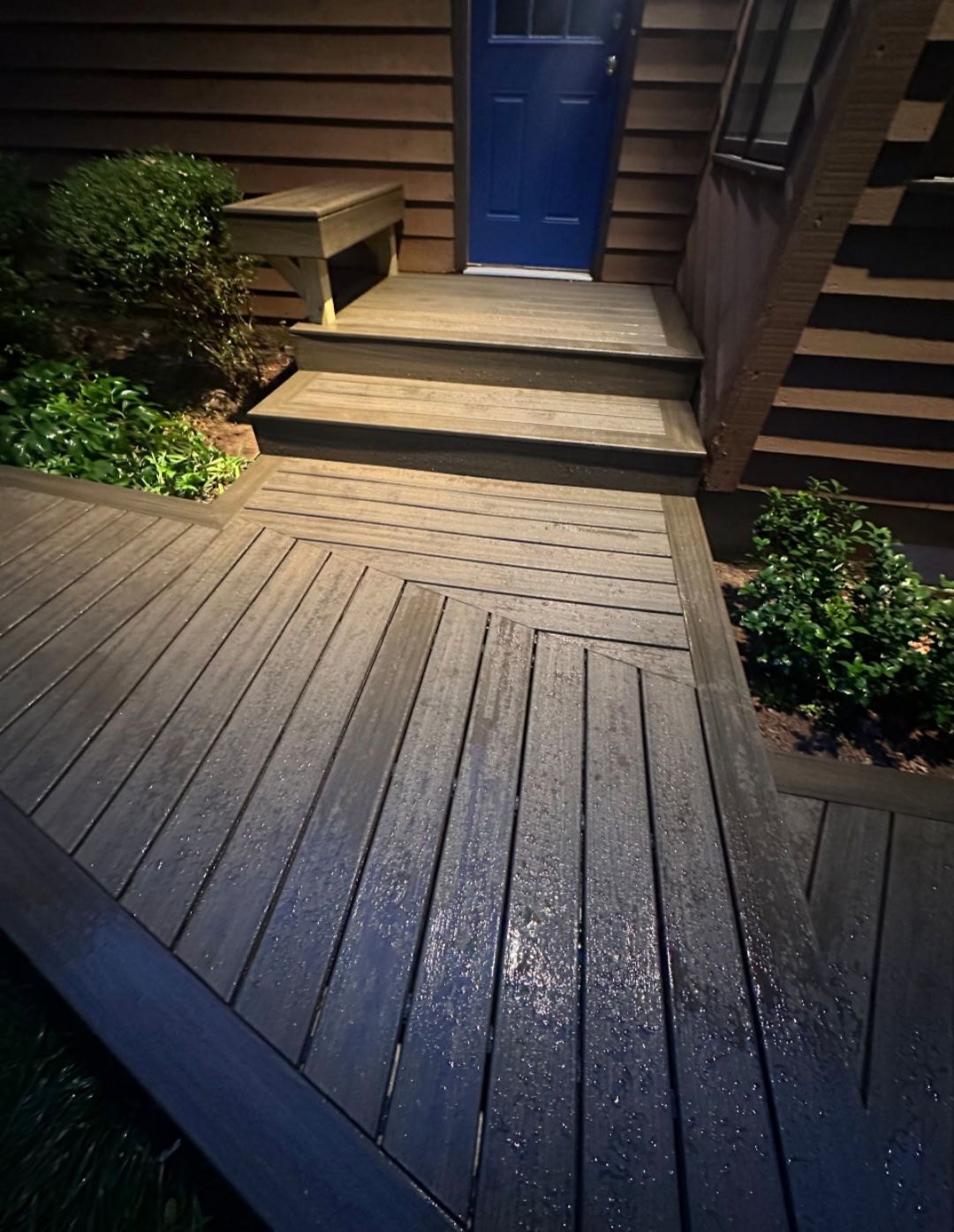 Front entry composite deck with herringbone inlay pattern and dark steps to a blue front door at night