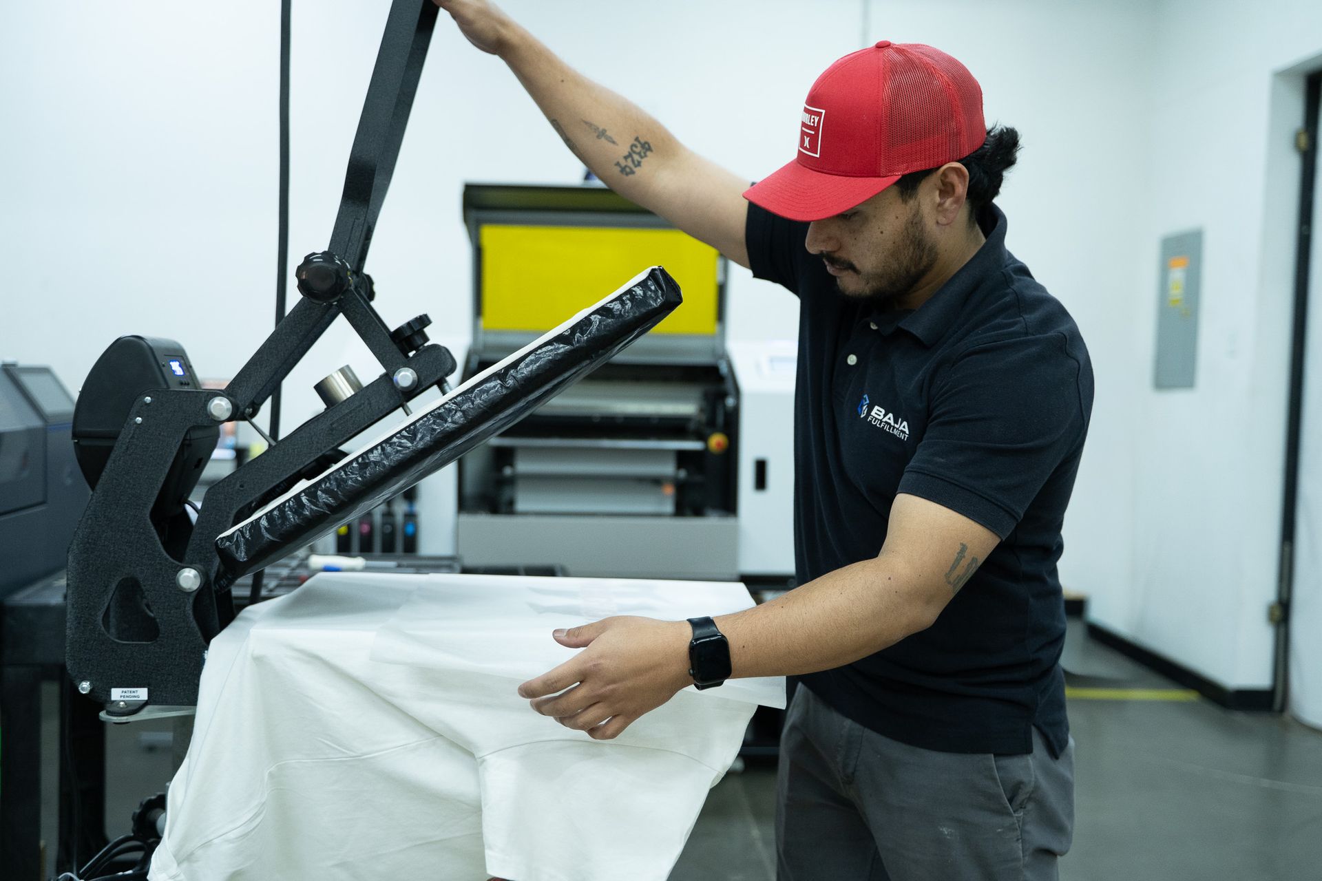 Man adjusting a black heat press machine on a worktable in a bright workshop