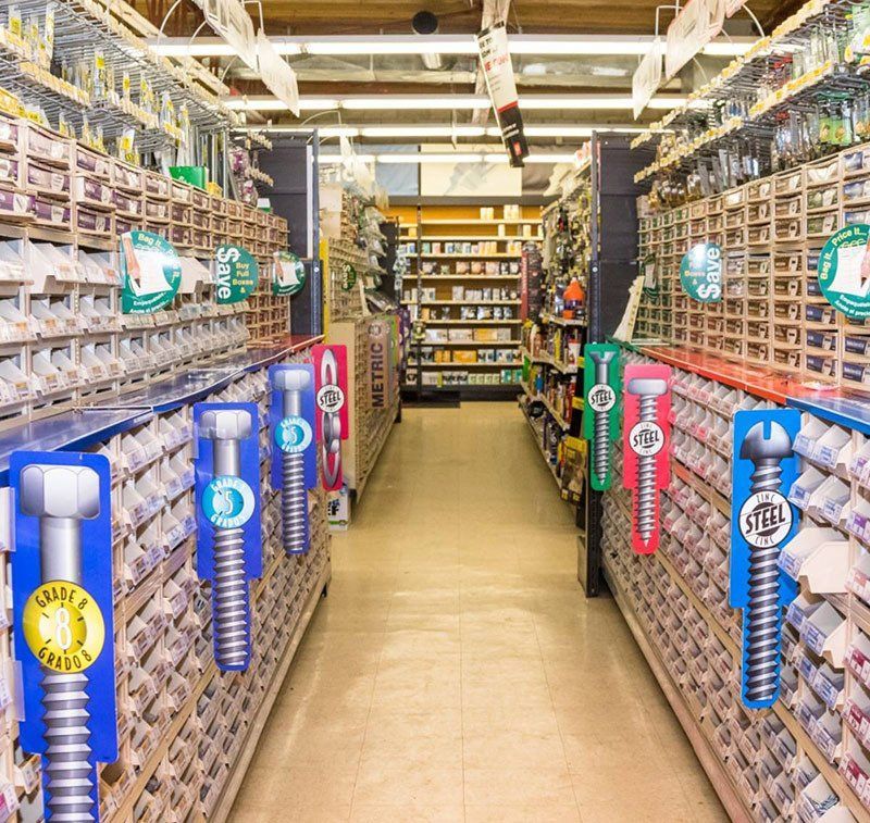 Hardware store aisle with shelving filled with bolts and hardware. Bolt-shaped signs hang throughout.