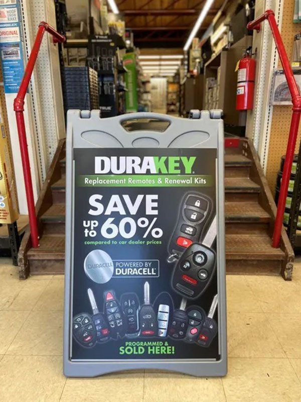 Gray sandwich board sign advertising DuraKey replacement keys, saving up to 60%, in a store aisle.