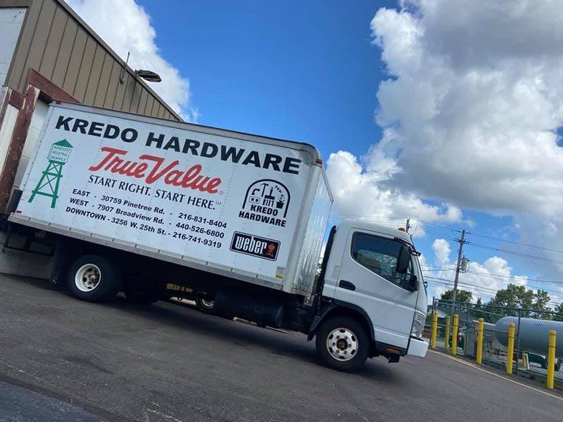 A white Kredo Hardware True Value delivery truck parked on a slight incline under a partly cloudy blue sky.