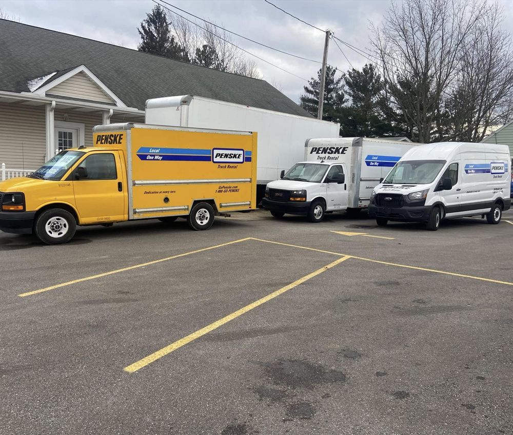 Yellow, white Penske trucks parked in a lot, in front of a building.