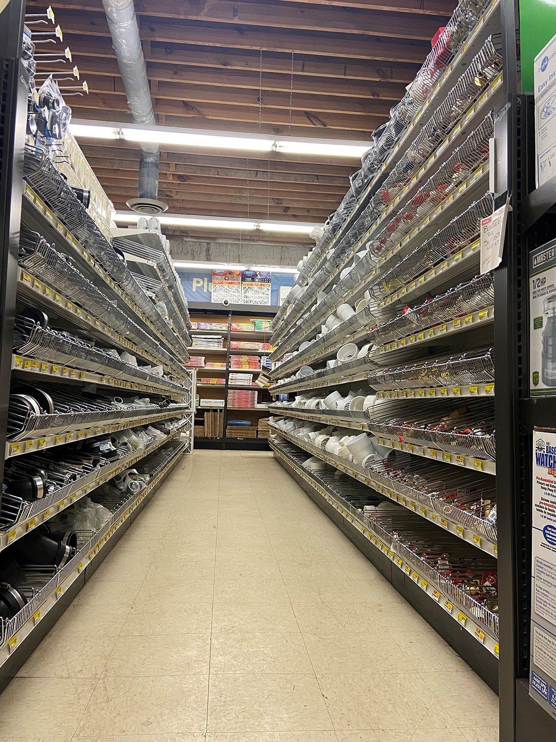 Rows of shelves stocked with hardware items in a store; an aisle leads towards the back.
