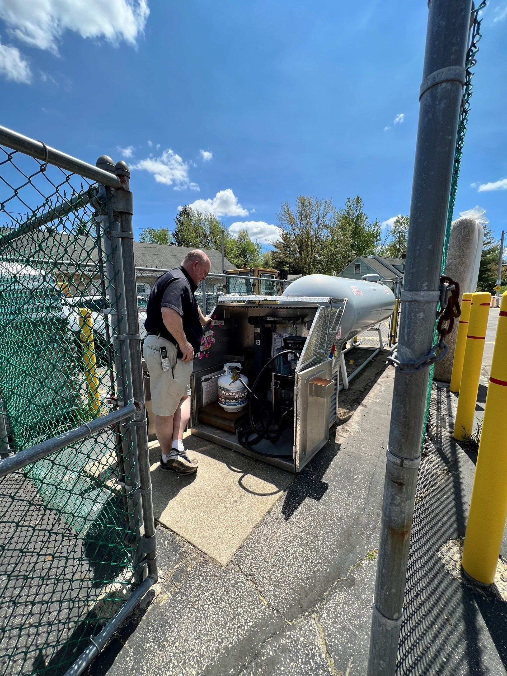 A person in a security uniform inspects equipment behind a chain-link fence on a sunny day.