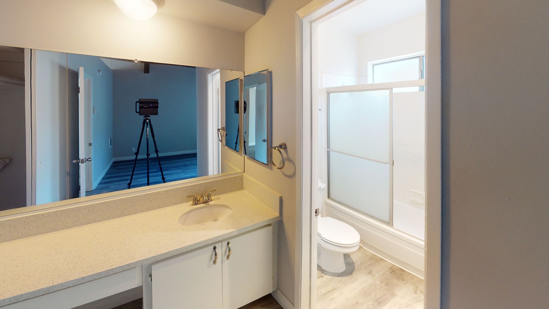 Bathroom with a vanity, toilet, and shower/tub combo.  A doorway leads to another room with a tripod.