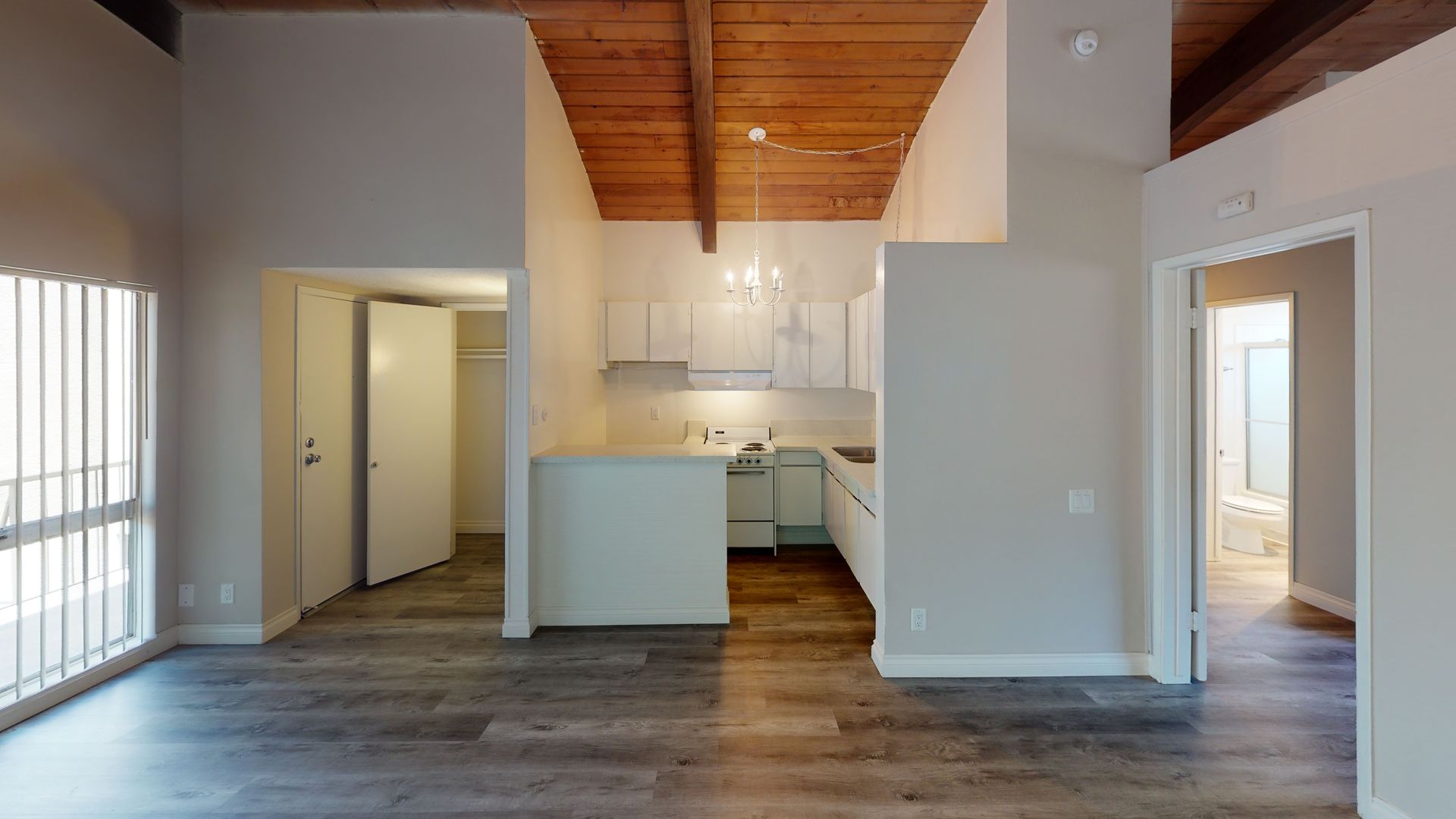 Interior view of a modern apartment with a kitchen, living area, and doors. Wooden ceiling, gray floors.