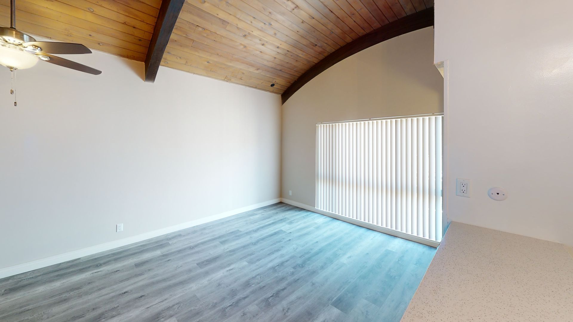 Empty living room with wood ceiling, vertical blinds, and gray flooring.