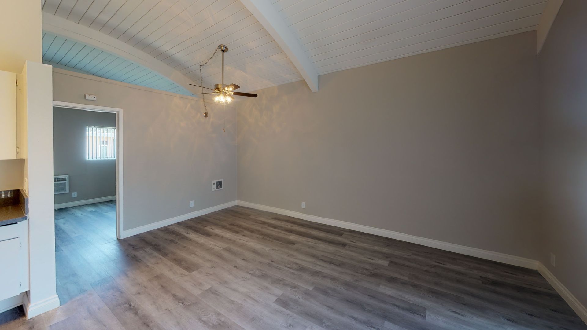 An empty room with a vaulted ceiling, gray walls, and wood-look flooring. A doorway leads to another room.