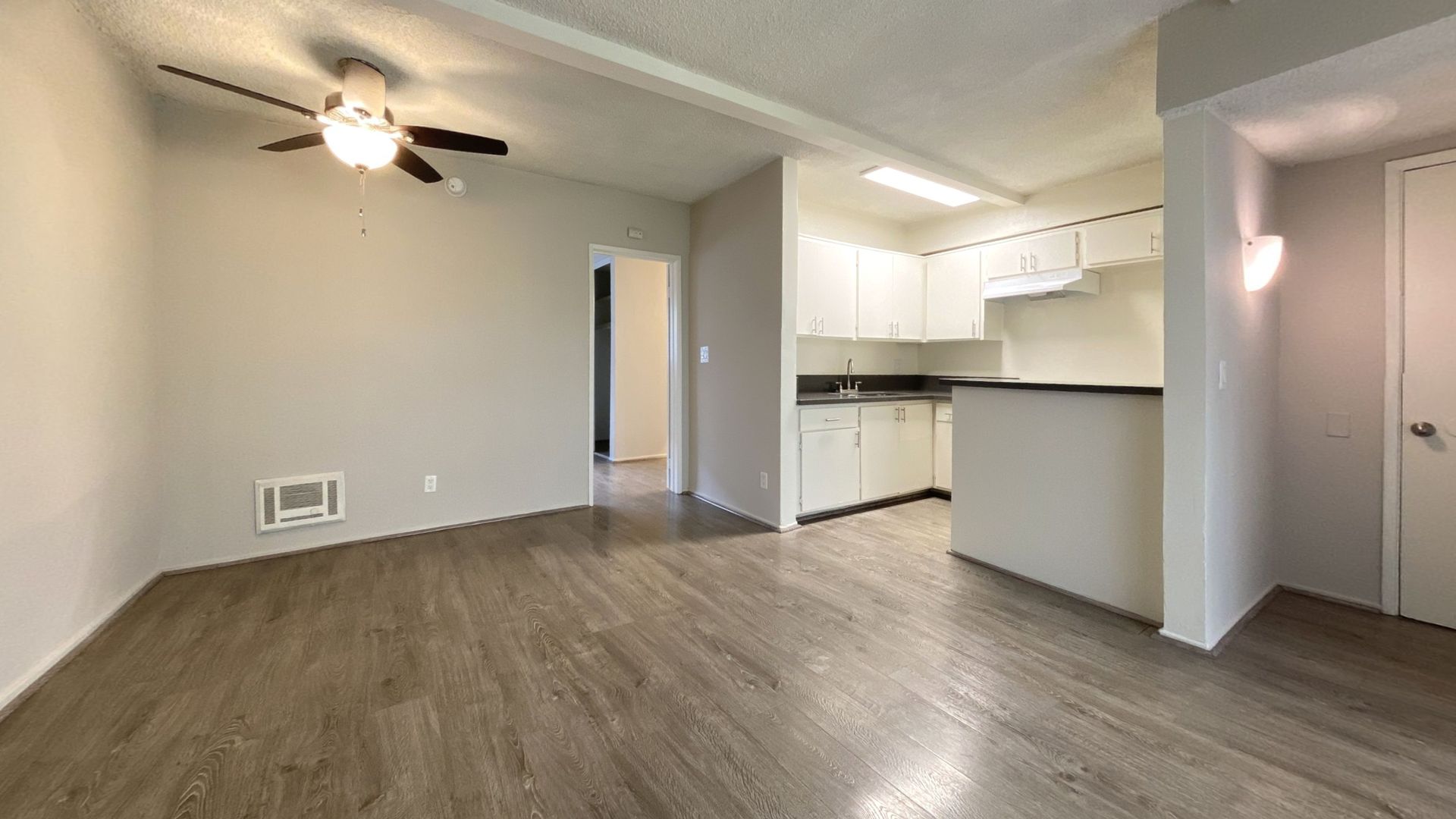 Empty apartment interior with wooden floor, kitchen, and open doorways.