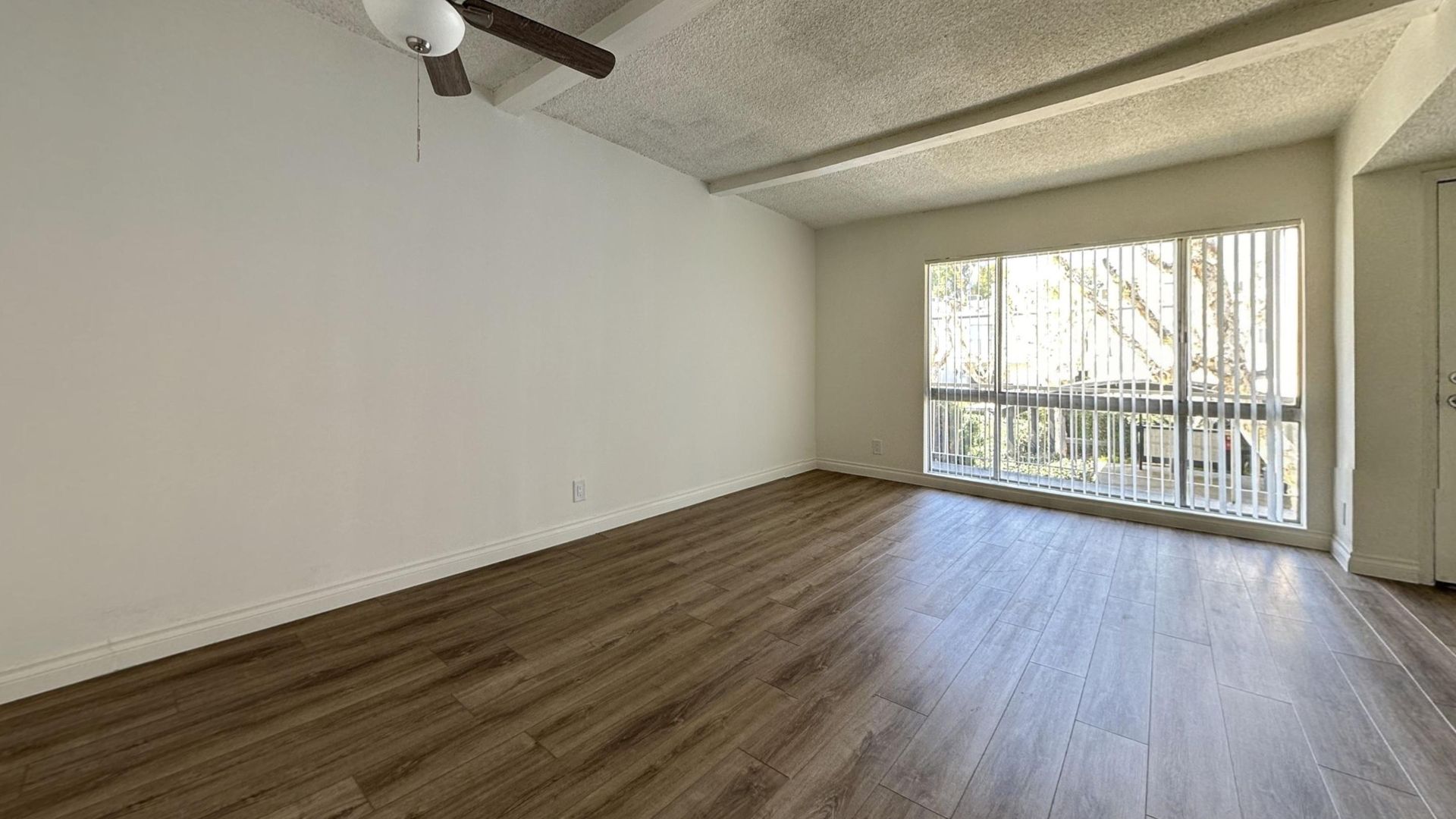 Empty room with wood floors, large window, ceiling fan, and white walls.