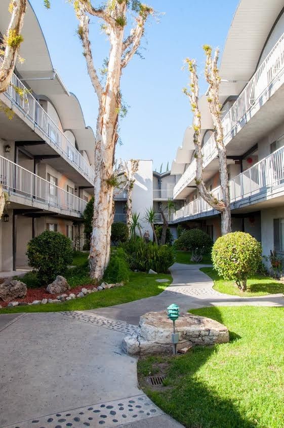 Courtyard of a two-story apartment building with green grass, trees, and a stone pathway.