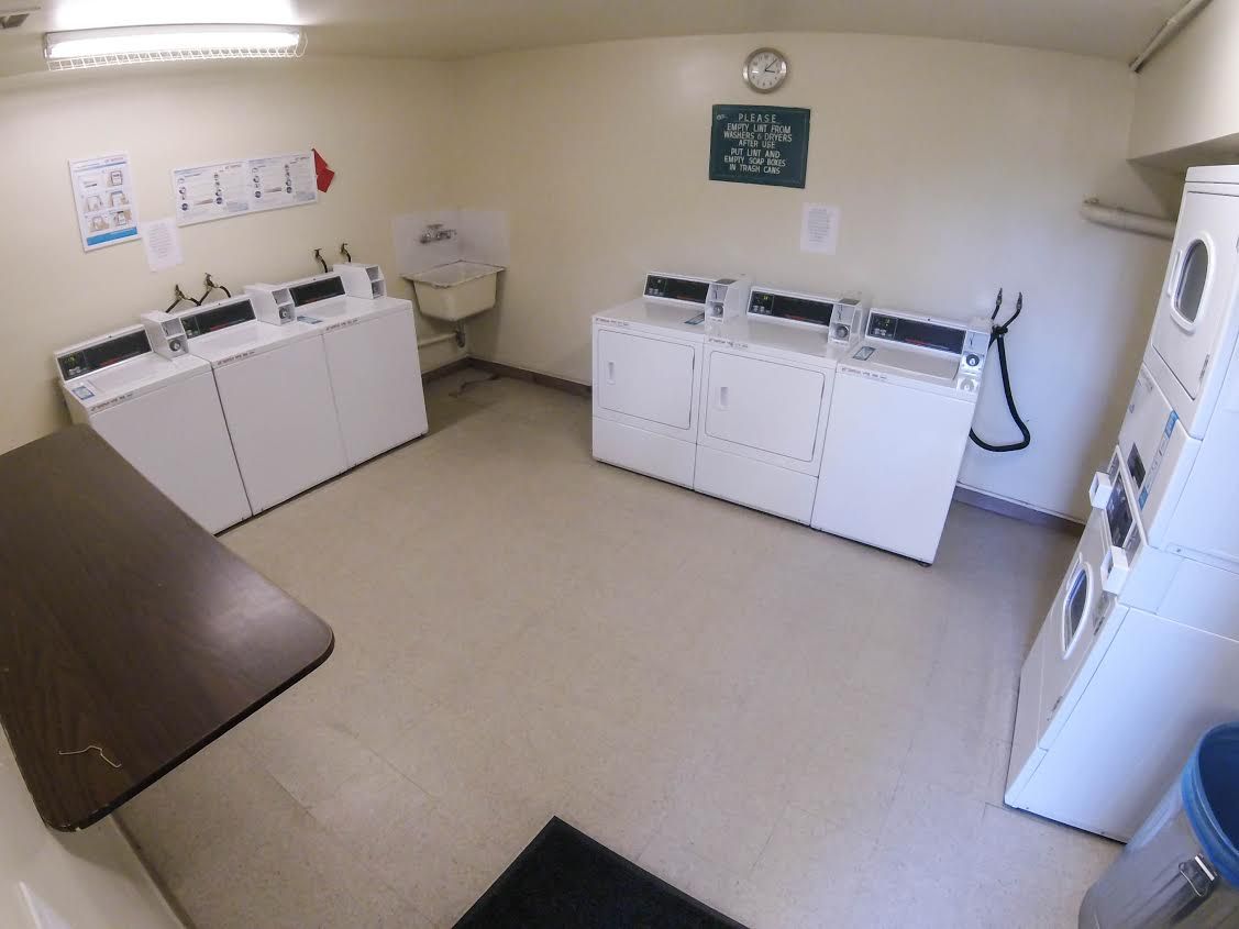 Laundry room with several white washing machines and a sink.