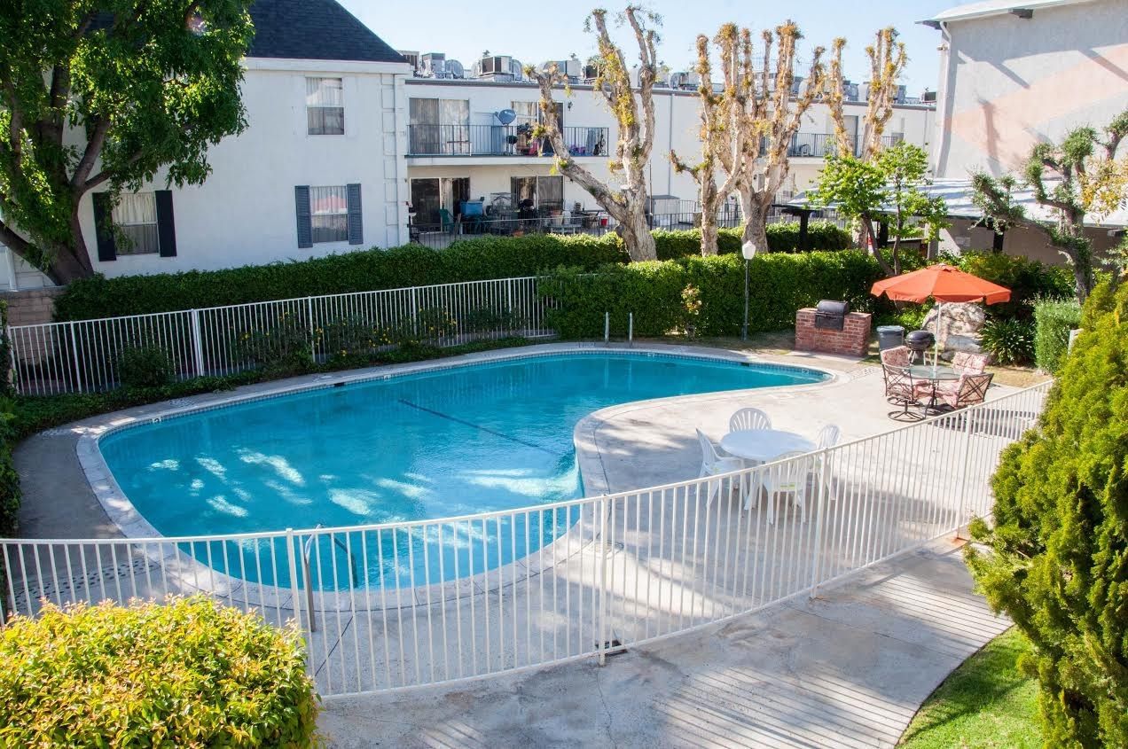 Pool with cover and surrounding apartments, small table with chairs, red umbrella.