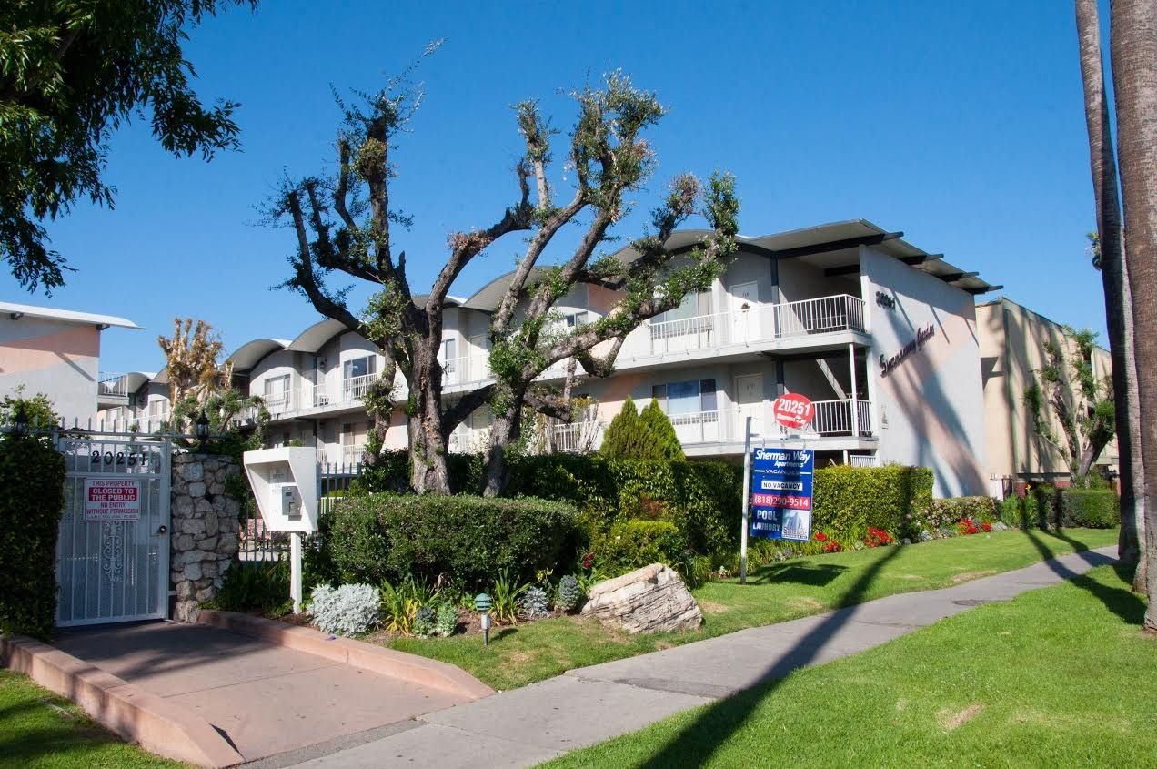 Multi-story apartment building with green lawn and trimmed bushes.