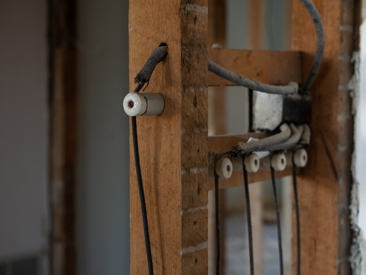 Exposed electrical wiring on wooden framing. A fuse is visible, with black and gray wires in a construction setting.