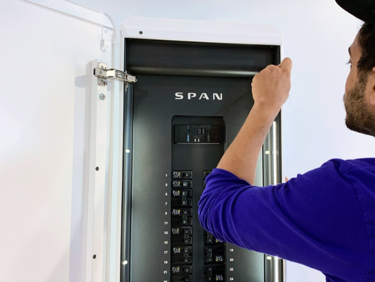 Person opening the door of a Span smart electrical panel, indoors.