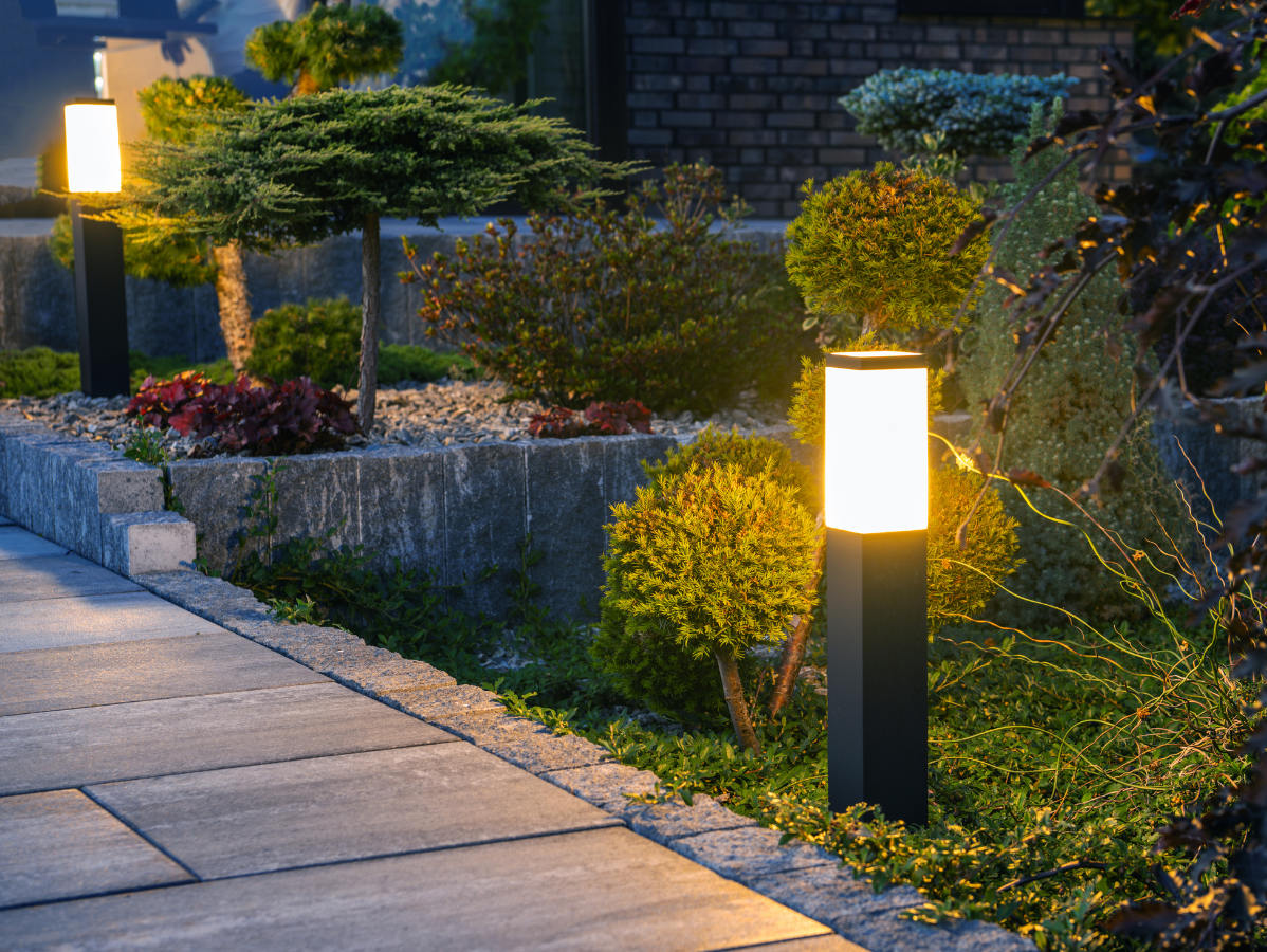 Illuminated garden path with modern black lights, stone walkway, and manicured bushes.
