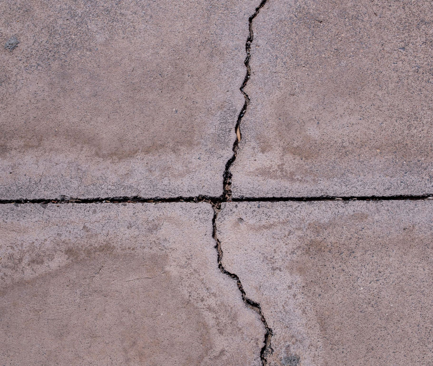 An image of a worker pouring asphalt on the cracked concrete driveway.