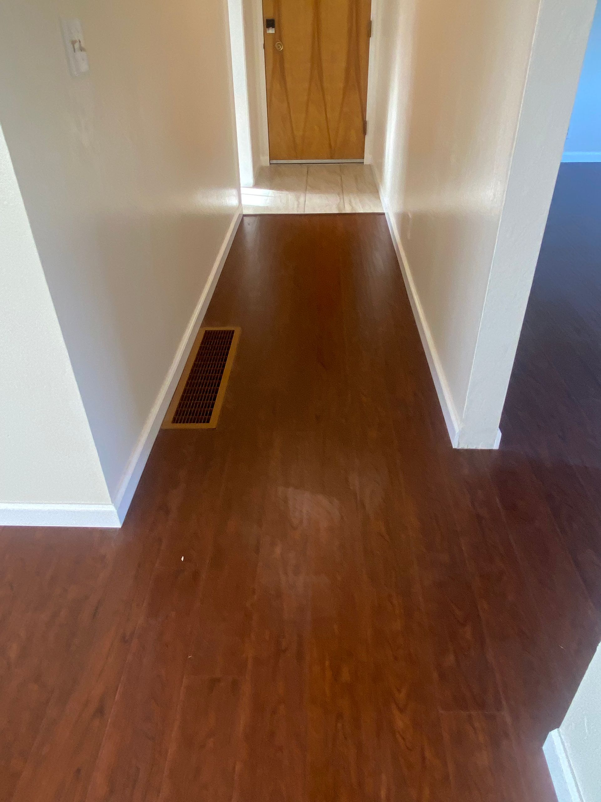 A hallway with hardwood floors and a door.