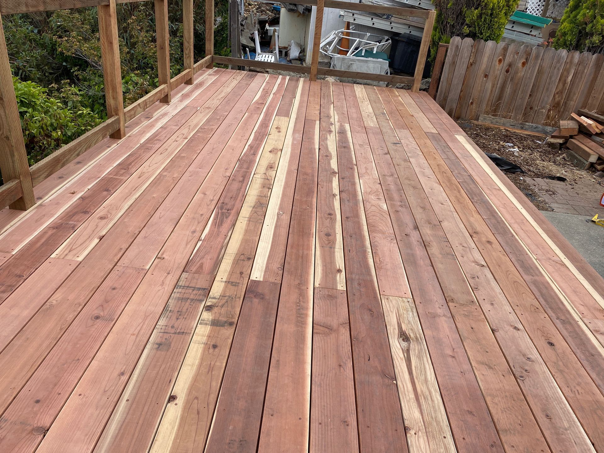 A wooden deck with a fence in the background is being built.