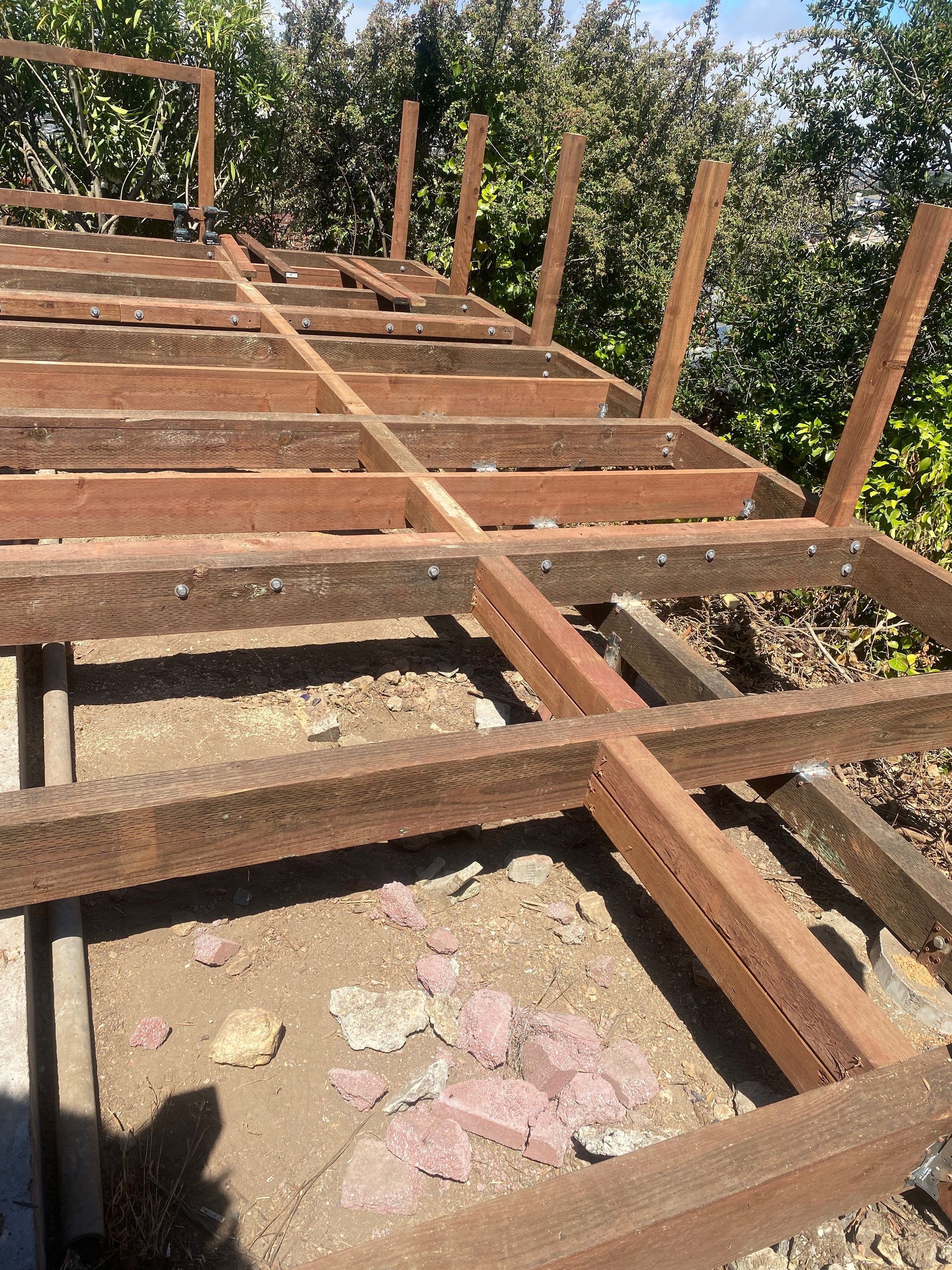 A wooden structure is being built in the dirt with trees in the background.