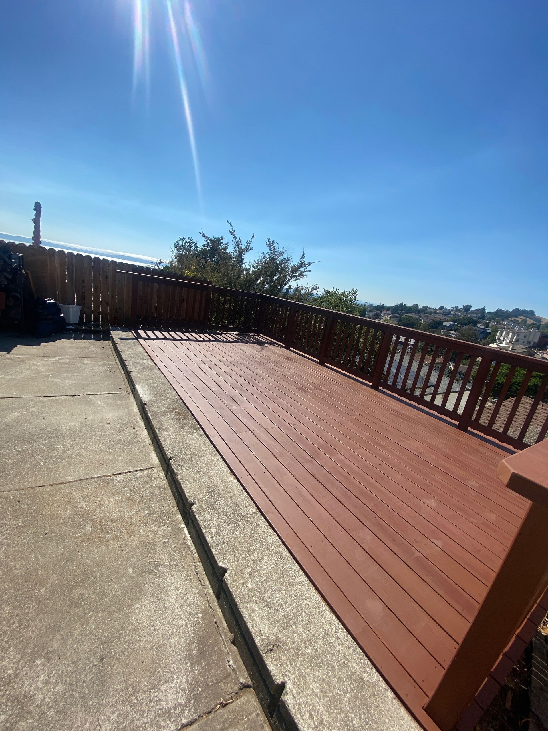 A red wooden deck with a fence and a view of a city.
