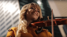 A woman in a yellow sweater is playing a violin.