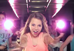 A girl in a pink tank top is dancing in front of a group of people.