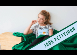 A woman is sitting on a green blanket with a green ribbon that says jade pettyjhon