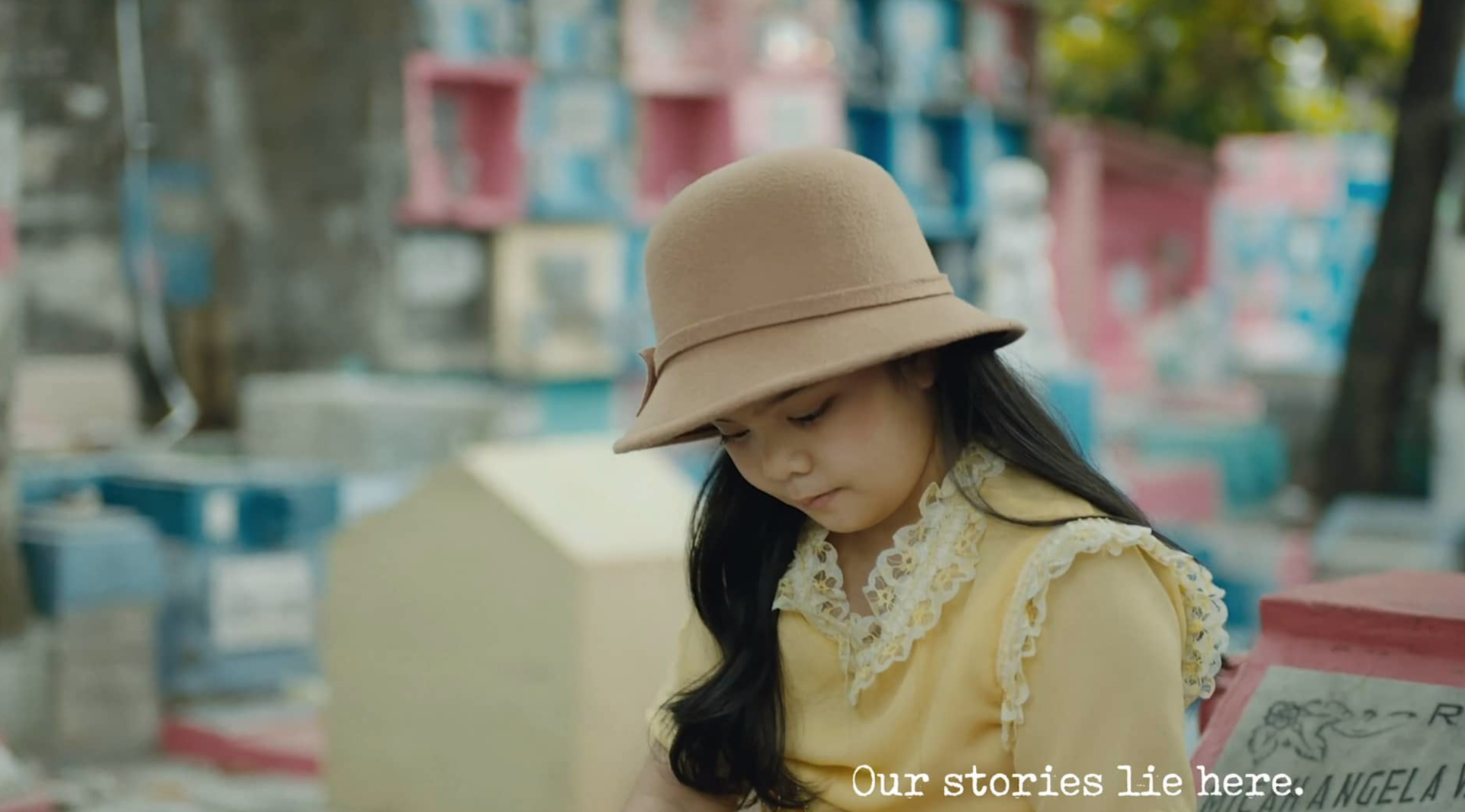 A young girl wearing a hat is sitting in a cemetery.