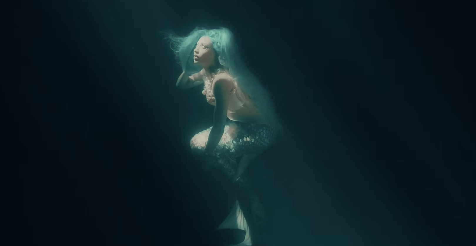 A mermaid is swimming underwater in the dark.