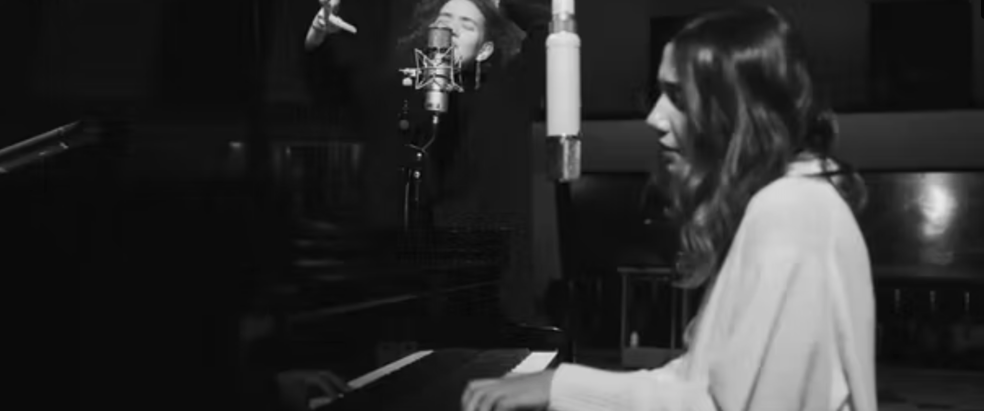 A woman is playing a piano and singing into a microphone in a black and white photo.