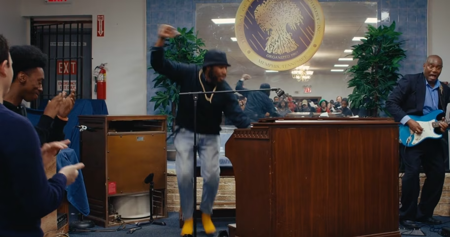 A man is dancing in front of a microphone in a room while another man plays a guitar.