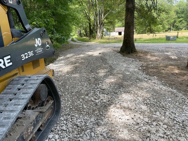 Tracked construction vehicle on a gravel path beside trees and a grassy park area