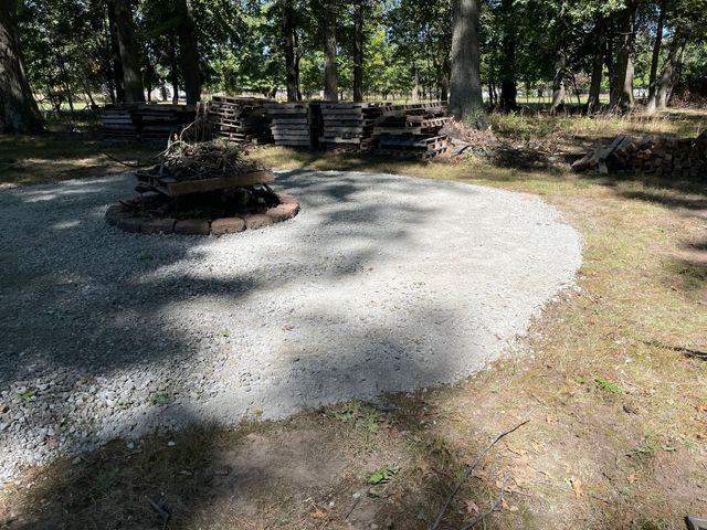 Gravel campsite with a stone fire ring and picnic tables under trees in a wooded park