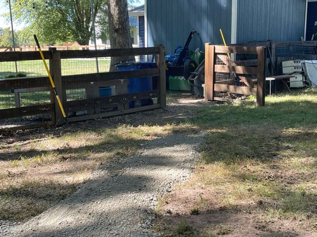 Gravel path leading to a blue barn and wooden gate in a sunny yard